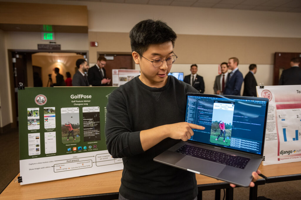 Chico State student shares details about his GolfPose app on laptop at a showcase. 