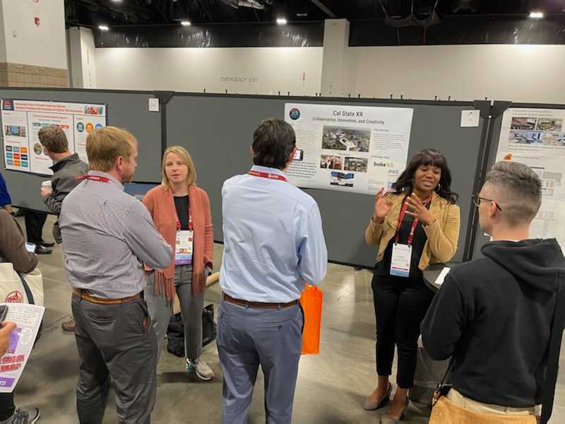 Kate Miffitt and Allison Green talking with visitors about  Cal State XR in front of a poster. 
